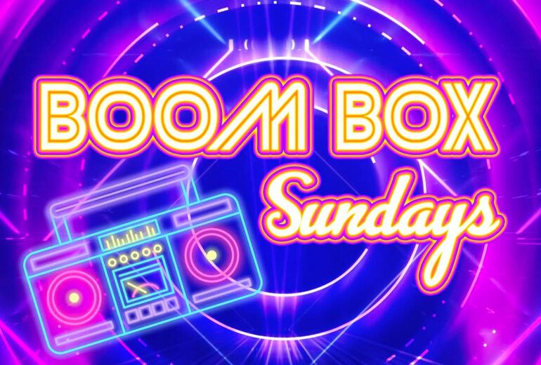 A neon-themed graphic featuring the words "Boom Box Sundays" in bold, bright yellow and orange lettering. A glowing neon boombox is placed below the text, surrounded by swirling purple and blue lights.