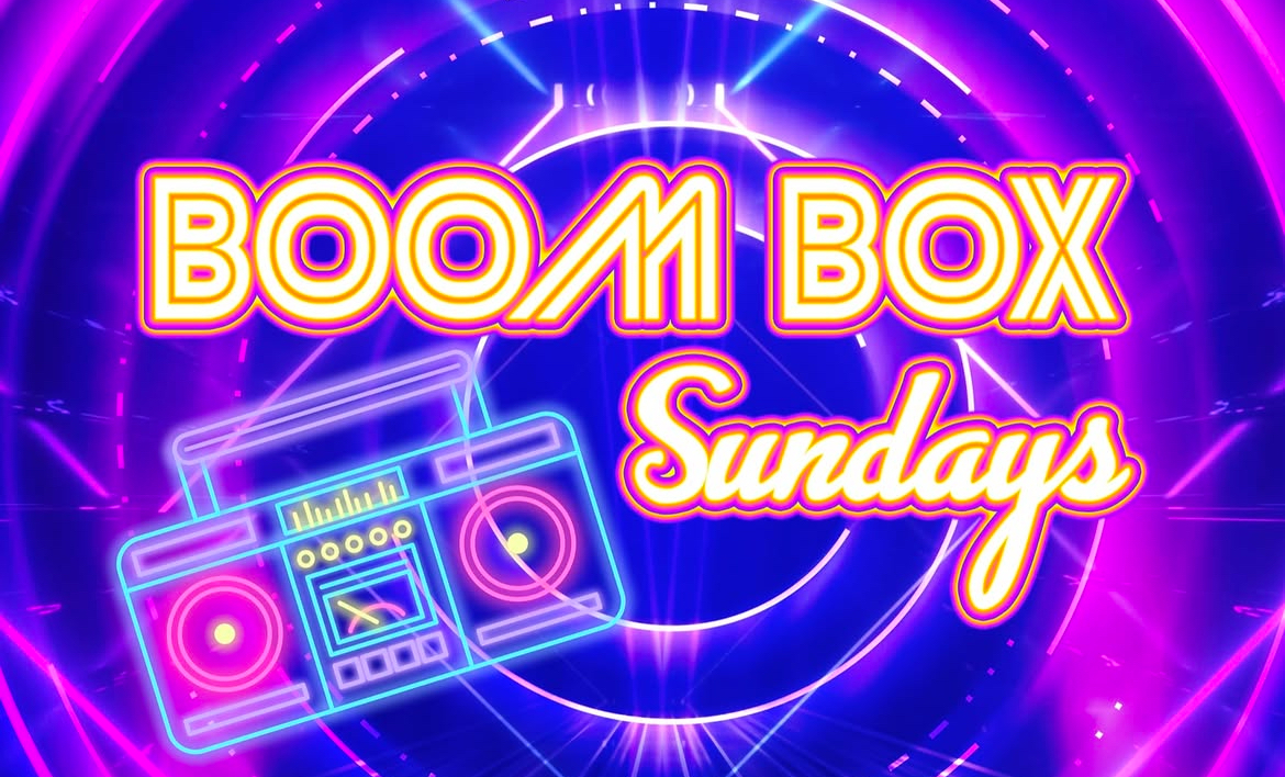 A neon-themed graphic featuring the words "Boom Box Sundays" in bold, bright yellow and orange lettering. A glowing neon boombox is placed below the text, surrounded by swirling purple and blue lights.